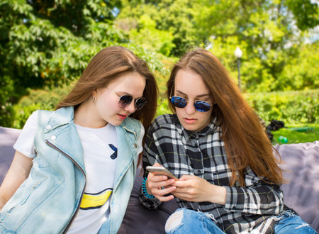 Two young women in the park looks at the phoneの写真素材