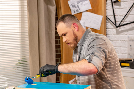 profession, carpentry, woodwork and people concept - carpenter working with wood plank and covers it with paint at workshopの写真素材