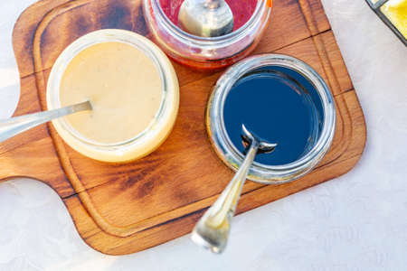 Spoon with tasty sweet sauces and jar on board, condensed milk, honey, jamの写真素材
