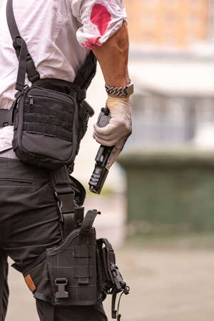 man dressed in a bulletproof vest, a shirt in his blood, pursues a victim with a gunの写真素材