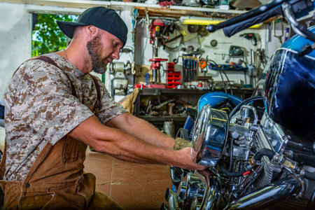 Side view portrait of man working in garage repairing motorcycle and customizing itの写真素材