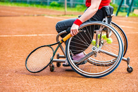 Disabled young woman on wheelchair playing tennis on tennis court.の写真素材