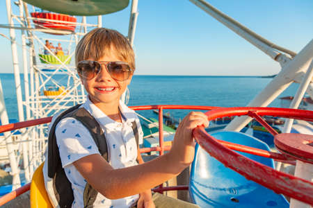 Smilling excited boy in glasses enjoying the view from ferris wheel in amusement parkの写真素材