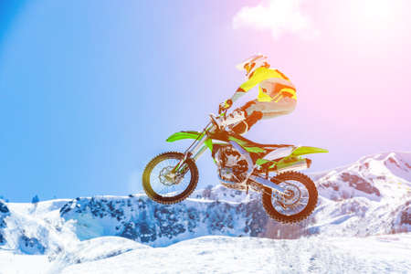 racer on a motorcycle in flight, jumps and takes off on a springboard against the snowy mountainsの写真素材