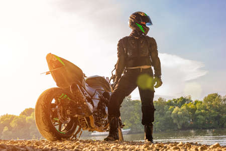 Man wearing motorcycle helmet and safety uniform sitting on bike outdoors, beautiful scenic landscape on the background in daytime setting.の写真素材