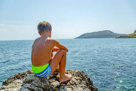 Boy on the beach stones. against the background of clear sea waterの写真素材
