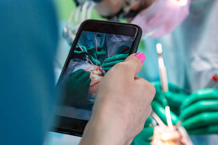 Surgeons operating a patient in an operating theater in a hospital while assistant makes photo on a mobile phone cameraの写真素材