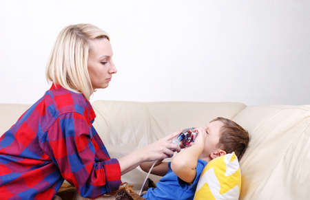 Boy breathe through nebulizer Mother holds a nebulizer mask in the boys face during inhalation. Sick chid with pediatric nebulizer.の写真素材