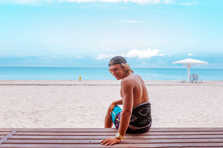 The surfer sits on the terrace on the beach with his back to the camera and turn the face looking to the cameraの写真素材
