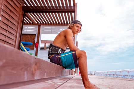 The surfer sits on the terrace on the beach and looking to the camera. Side view