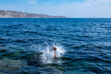 A boy is jumping from the cliff into the sea wiht big water splash on a hot summer day. Holidays on the beach. The concept of active tourism and recreationの写真素材