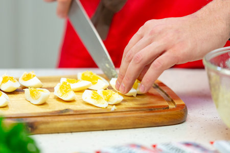 Man cuts boiled quail eggs on wooden cutting board close-up. Step by step recipe of homemade tuna salad.の写真素材