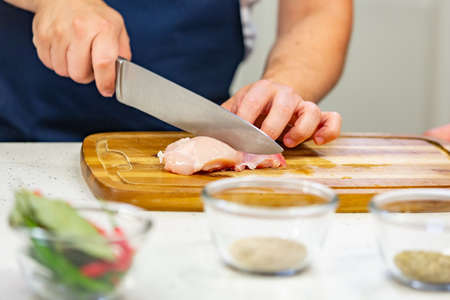 Mens hands cut raw chicken on the wooden board close upの写真素材