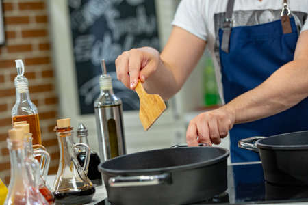 Man cooks meat in a frying pan. Hand using spatula to stir frying pan full of meat.の写真素材