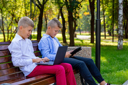 Teenage Boys On Park Bench Using Laptop And Digital Tabletの写真素材