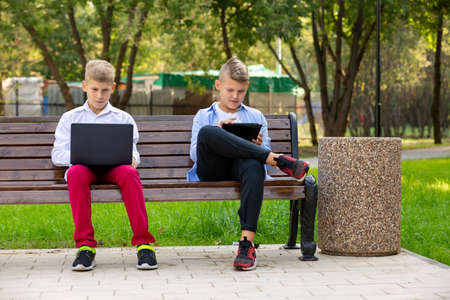 Teenage Boys On Park Bench Using Laptop And Digital Tabletの写真素材