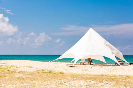 The sun loungers under the big sun shade on the idyllic beach. white tent on the beach.の写真素材