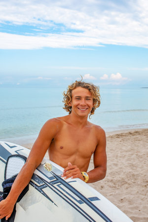 Handsome man walk with white blank surfing board wait for wave to surf spot at sea ocean shore. Concept of sport, fitness, freedom, happiness, new modern life, hipster.の写真素材