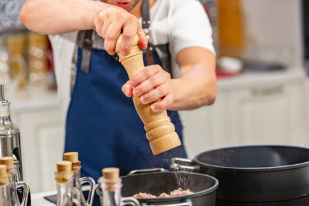 man adds ground pepper from the mill into frying pan on stove. ooking concept