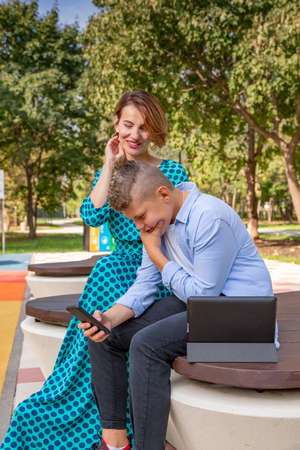family, augmented reality, technology and people concept - mother and her son sitting on a park bench and enjoy the phoneの写真素材