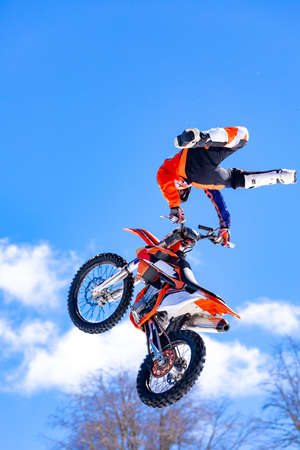Racer on a motorcycle in flight, jumps and takes off on a springboard against the snowy mountainsの写真素材