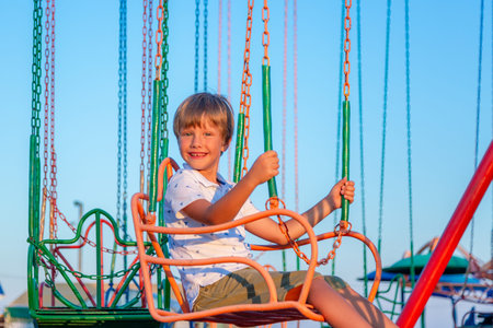 Happy child boy having fun in amusement park. Taking a ride on chain carousel.の写真素材