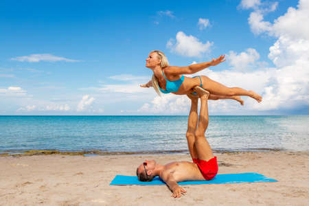 young couple woman and men on the beach doing fitness yoga exercise together. Acroyoga element for strength and balanceの写真素材