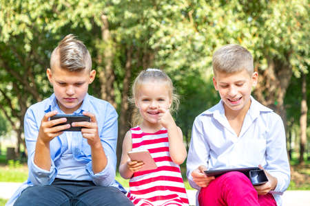 busy kids looking at their phones texting sms and playing sitting outsideの写真素材