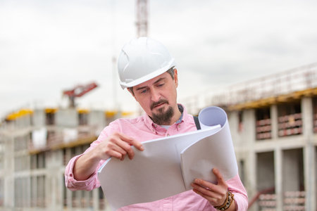 Portrait of architect at work with helmet in a construction site, reads the plan, paper projectsの写真素材