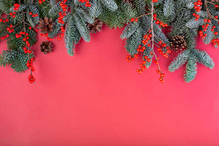 Christmas composition. Christmas red decorations, fir tree branches with bumps on red background. Flat lay, top view, copy spaceの写真素材