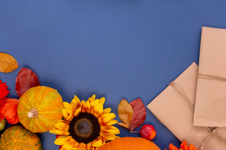 Top view of handcraft gift box with yellow and orange flowers, rope reel and pumpkins on blue...