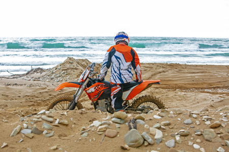 Motorcyclist in a protective suit sitting on motorbike in front of the sea