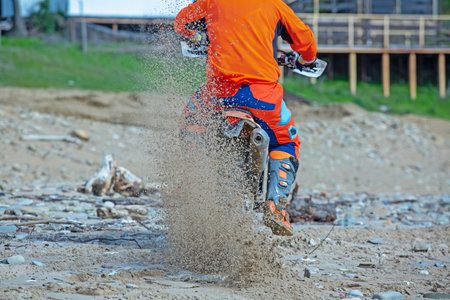 Motorcyclist in a protective suit rides a motorcycle on the sea, splashes fly from under the wheels.