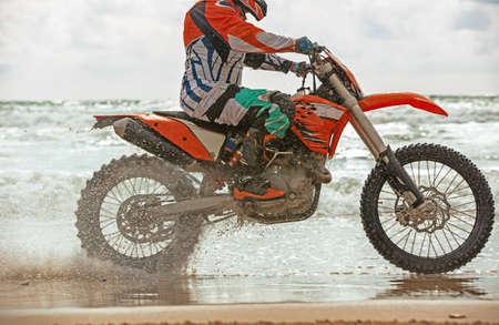 Motorcyclist in a protective suit rides a motorcycle on the sea, splashes fly from under the wheels.の写真素材
