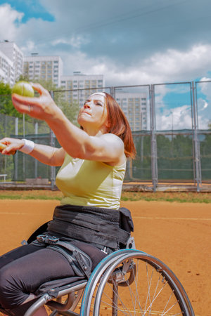 Disabled young woman on wheelchair playing tennis on tennis court.