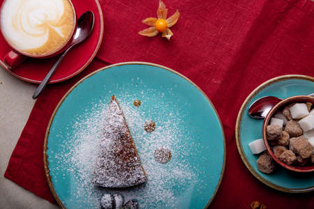 Piece of carrot cake, covered with powdered sugar in a blue plate on a red napkin with cup of coffe and brown sugarの写真素材