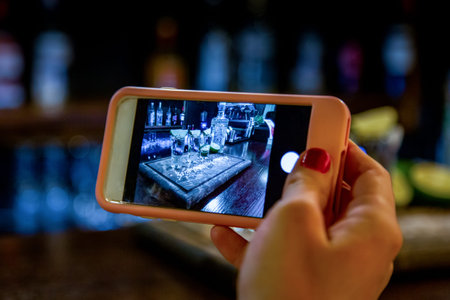 Hand with smartphone taking a photo of alcoholic shots of tequila in the bar