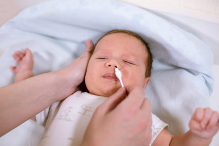 Newborn hygiene. Mother cleaning baby nose with cotton swab, closeup