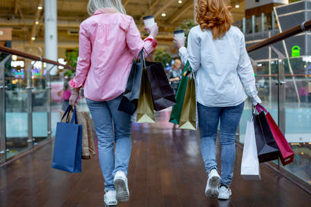 Happy young women with shopping bags enjoying in shopping, girls are having fun with their purchases. rear view. Consumerism and lifestyle conceptの写真素材