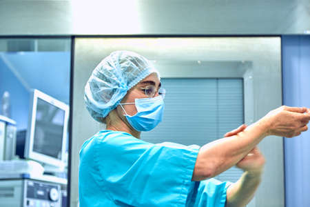 Female Surgeon in a medical mask and in a suit in the hospital washing thoroughly her hands before performing a surgeryの写真素材