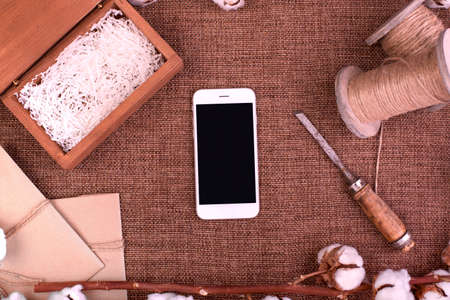 Flower design with fluffy dried cotton bolls gift boxes, white smartphone and jute rope hank over rough brown burlap Top view copy space greeting cardの写真素材