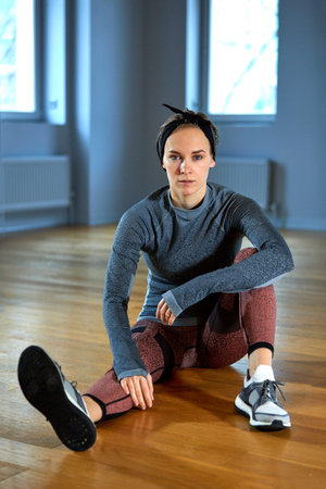 beautiful fit woman in sportswear posing while sitting on the floor in front of window at gym