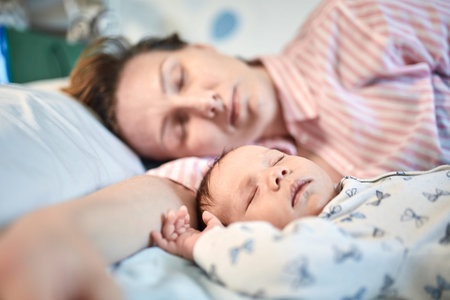 Portrait of newborn baby and mother sleeping on bed, resting togetherの写真素材