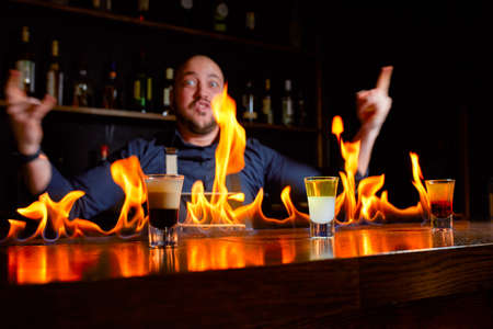 Fiery show at the bar. The bartender makes hot alcoholic cocktail and ignites bar. Bartender prepares a fiery cocktail. Fire on bar.の写真素材