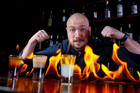 Fiery show at the bar. The bartender makes hot alcoholic cocktail and ignites bar. Bartender prepares a fiery cocktail. Fire on bar.の写真素材