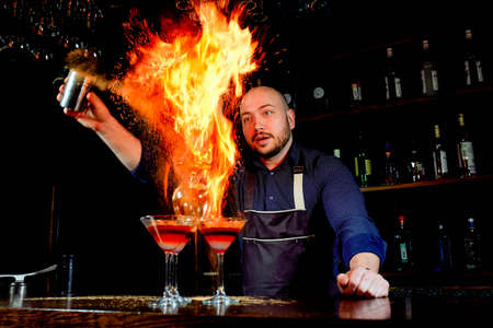 Fiery show at the bar. The bartender makes hot alcoholic cocktail and ignites bar. Bartender prepares a fiery cocktail. Fire on bar.の写真素材