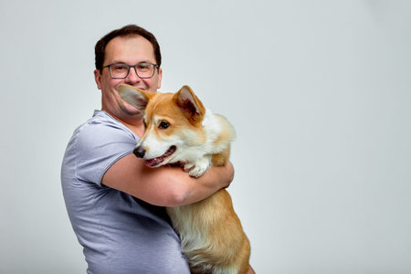The dog lies on the shoulder of its owner.Welsh Corgi in his owners hands on white background. The concept of people and animals.の写真素材