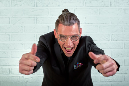 Close up portrait of a happy young businessman wearing glasses dressed in a black suit shows hands...