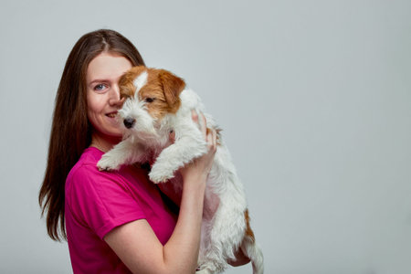 Beautiful girl with a jack russell terrier on her hands on a gray background, copy space