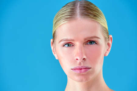 Beauty Woman face Portrait. Beautiful Spa model Girl with Perfect Fresh Clean Skin. Blonde female looking at camera and smiling. Youth and Skin Care Concept. Blue background grayの写真素材